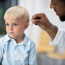 A doctor fits a young child with a hearing aid.
