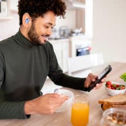 Young man with a hearing aid checking his phone over breakfast.